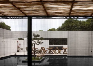 A minimalist terrace with wooden tables and chairs surrounded by greenery.