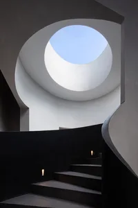 Concrete staircase with black railings and a circular skylight in the ceiling.