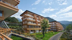 A modern apartment complex with wooden frame exteriors and balconies. Mountain landscape in the background.