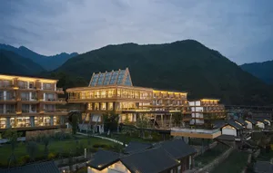 A modern resort with wooden frame and glass features, set against a mountainous backdrop.