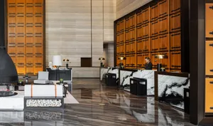 A modern hotel lobby featuring marble and concrete finishes, with a receptionist desk and seating area.