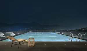 A modern rooftop pool illuminated at night, featuring a glass barrier and a view of distant mountains.