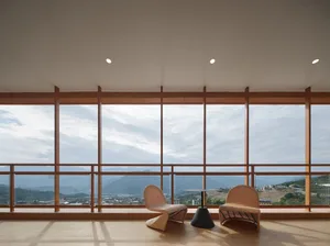 Two wicker chairs and a black table with a glass top overlooking a scenic landscape through large glass windows.