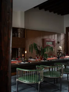 A modern dining room featuring wooden tables and chairs with green leather cushions. Table is set with red wine glasses and b