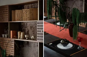 A modern dining room features ceramic crockery, hanging green plants, and a red table runner on a wooden table.