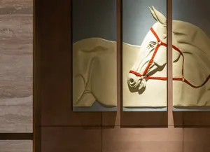 A detailed plaster sculpture of a horse, with a red harness on its head, mounted on a wooden wall.