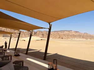 Person standing on a patio with a desert landscape in the background, featuring textile sails, concrete pillars, and a modern