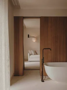 Modern minimalist bathroom with white freestanding bathtub, wooden paneling, and white floor tiles.