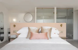 A minimalist bedroom with a white cotton mattress on a bed with a peach-colored bed frame, white cotton pillows, and peach-co