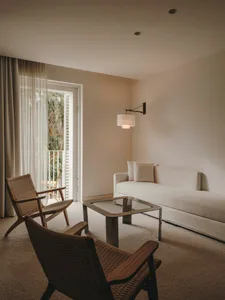 A minimalist living room with neutral-toned furnishings and a glass coffee table, featuring a door leading to a balcony.