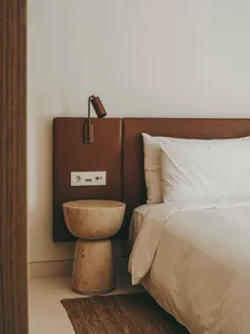 Modern minimalist bedroom featuring a bed with a brown leather headboard, white bedding, and a natural stone side table with 