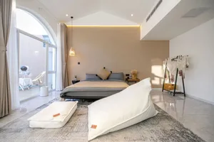 A minimalist bedroom featuring a bed with white pillows on a white floor, with a white arched window and a white arched rug.