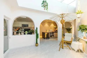 A minimalist kitchen with concrete flooring and walls, featuring modern appliances and a central island with bar stools.
