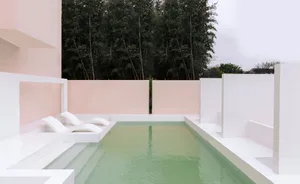 An outdoor minimalist poolside with concrete walls and a green pool.