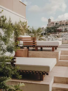 Modern minimalist outdoor rooftop lounge area with wooden benches and white cushions, overlooking a quaint European town on a