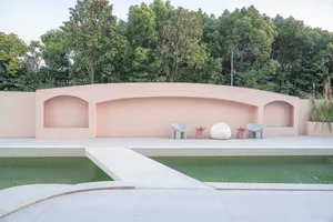 A minimalist swimming pool deck made from concrete, featuring a curved wall with arched cutouts and abstract seating arrangem