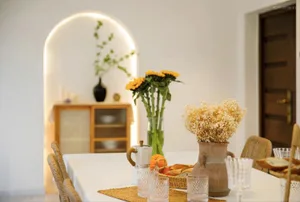 A well-designed dining room featuring a table adorned with ceramic vases, glasses, and a tray of bread and fruit, with a wood