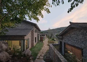 A modern residential villa with stone exterior and glass windows, surrounded by a natural landscape.
