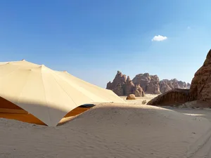 A modern tent structure in a desert landscape with a sandstone background.