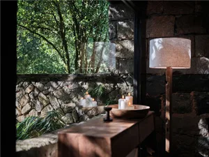 The image showcases a rustic living space featuring wooden furniture, stone walls, and a warm lighting arrangement.