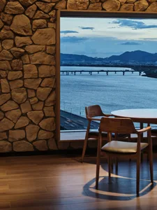 A restaurant interior with stone walls and wooden furniture overlooking a body of water.