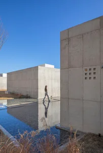 A modern building with a concrete exterior features clean lines and a minimalist design, surrounded by a large reflecting poo