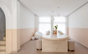 A minimalist dining room with a concrete table, white chairs, and light-colored walls and flooring.