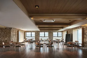 A spacious, modern restaurant cafe with round tables, wooden chairs, and stone walls, featuring a warm and inviting atmospher