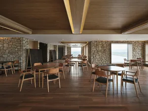 Interior of a restaurant cafe with wooden tables and chairs, stone accents, and large windows.