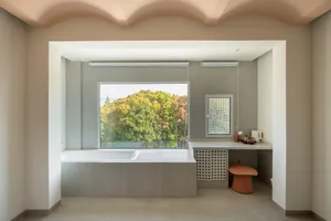 A modern bathroom featuring a minimalist design with concrete walls, a large window overlooking green trees, and a built-in b