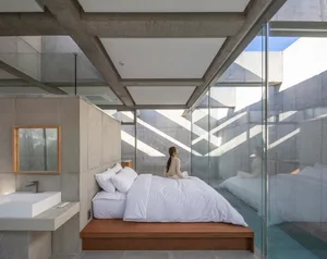 A minimalist bedroom with concrete walls, a wooden platform bed, and a white duvet.