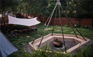 An outdoor wooden campfire pit surrounded by green vegetation and a white canopy.