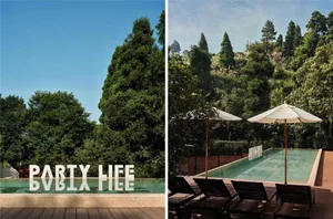 Concrete poolside resort with wooden deck, glass fencing, and lush greenery in the background.