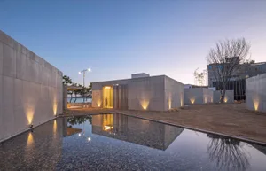 Modern minimalist exterior of a building with concrete walls and a reflection pool, illuminated by spotlights during twilight