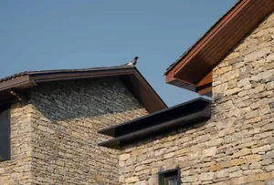 A close-up view of a modern stone building exterior with a bird sitting on the roof.