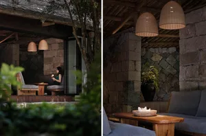 A cozy rustic living room with a wooden sofa, stone walls, and woven pendant lights.