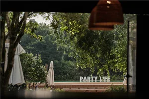 An outdoor party area with a sign reading 'PARTY LIFE' in front of a lush green backdrop.