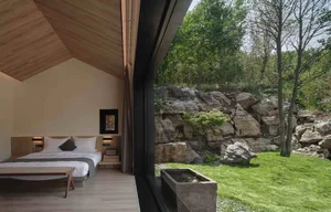 Minimalist bedroom with wooden elements and a view of natural surroundings.