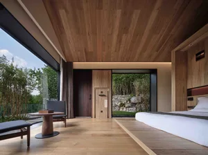 A modern bedroom with wooden walls and a large window overlooking greenery.