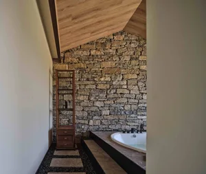 A modern residential bathroom featuring a stone wall, wooden ceiling, and a large soaking tub.