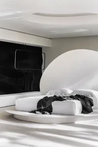 Modern black and white bedroom interior with concrete bed platform, white bedding, and matte black accents on the wall and ce
