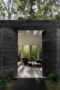 A modern black concrete entryway with a seating area indoors surrounded by greenery.