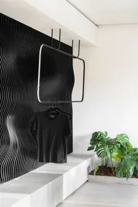Black metal clothing rack with wave-pattern on textured white wall and green plant in planter