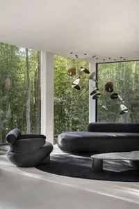 Modern living room featuring sleek, black furniture, large windows, and a hanging art installation