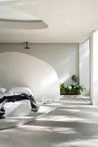 Minimalist bedroom with concrete flooring, white walls, and a round platform bed.