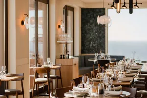 A beautifully designed coastal fine dining restaurant interior with wooden furniture, glass elements, and elegant lighting.