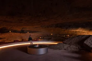 Person sitting on concrete seating area in a cave with rock formations and ambient lighting.