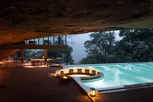 A luxurious resort with a swimming pool and circular seating area surrounded by a natural stone deck, overlooking a lush fore