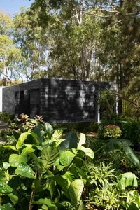 A minimalist black building surrounded by lush greenery in a forest setting.