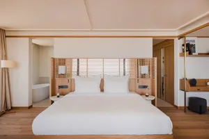 Minimalist hotel bedroom featuring a wooden bed with white bedding and a wooden headboard.